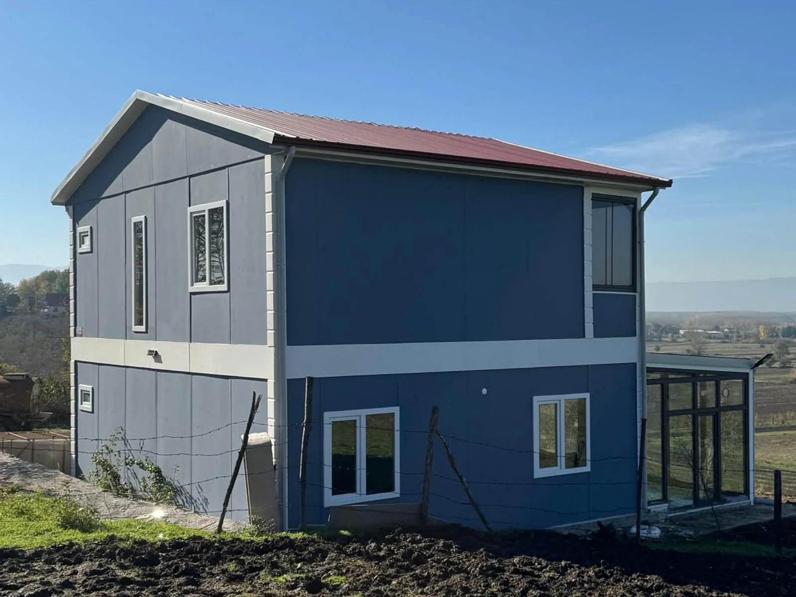 Çift katlı 3+1 prefabrik ev, lacivert cephe ve cam kış bahçesi eklentili kırsal dış görünüm